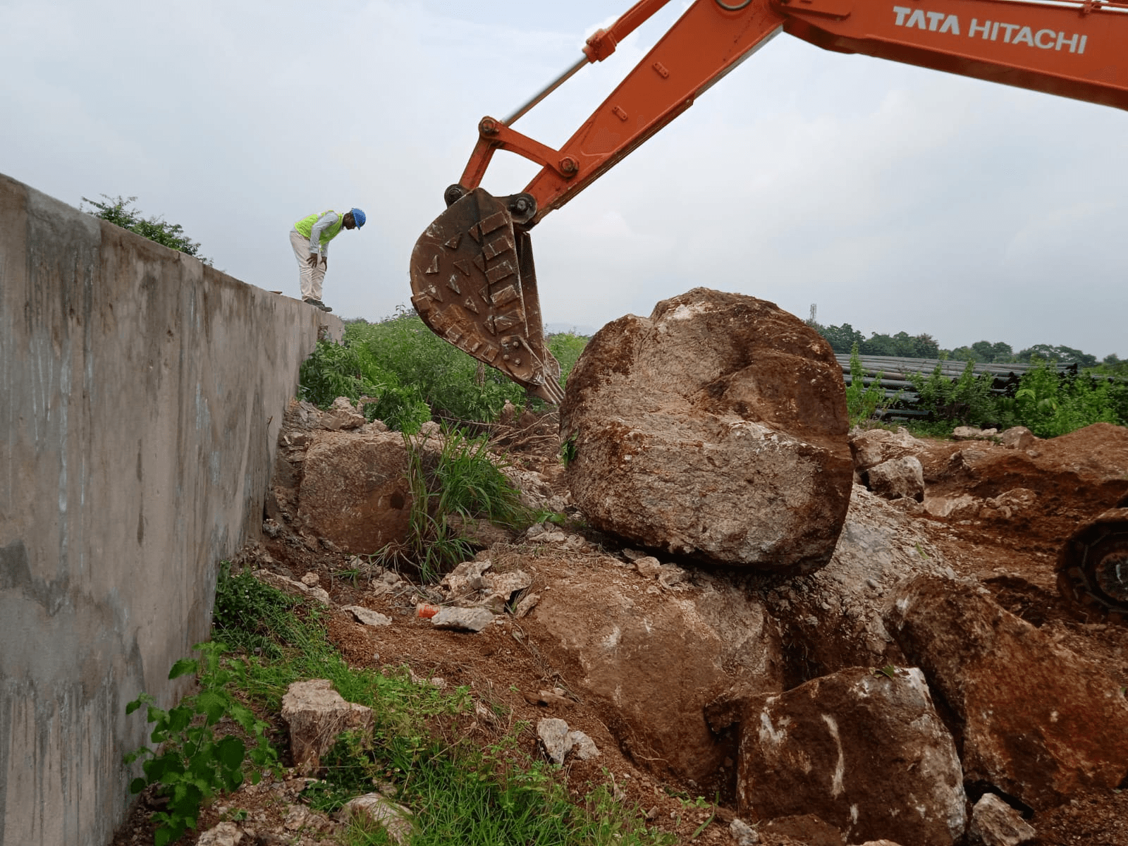 Excavator positioned beside a large boulder on an active site